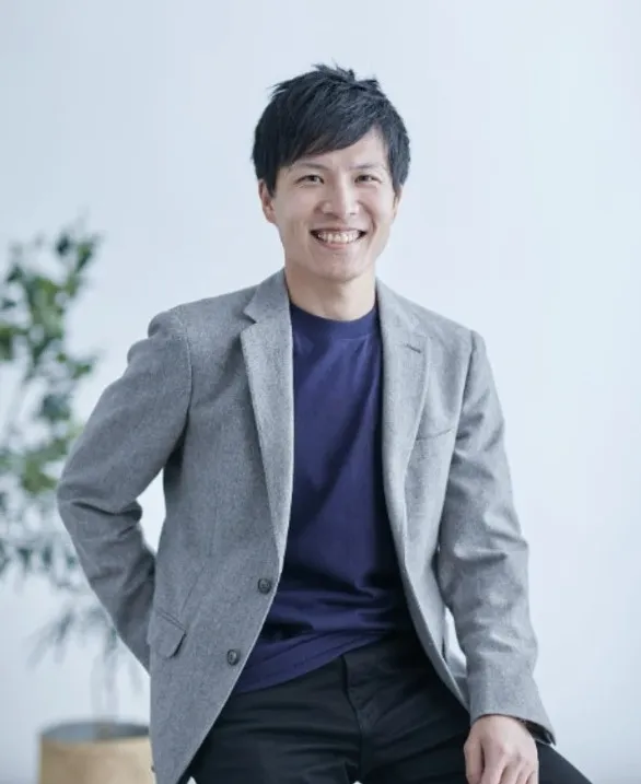 サイト管理者のプロフィール写真。グレーのジャケットと紺色のシャツを着た男性が笑顔でポーズを取っている